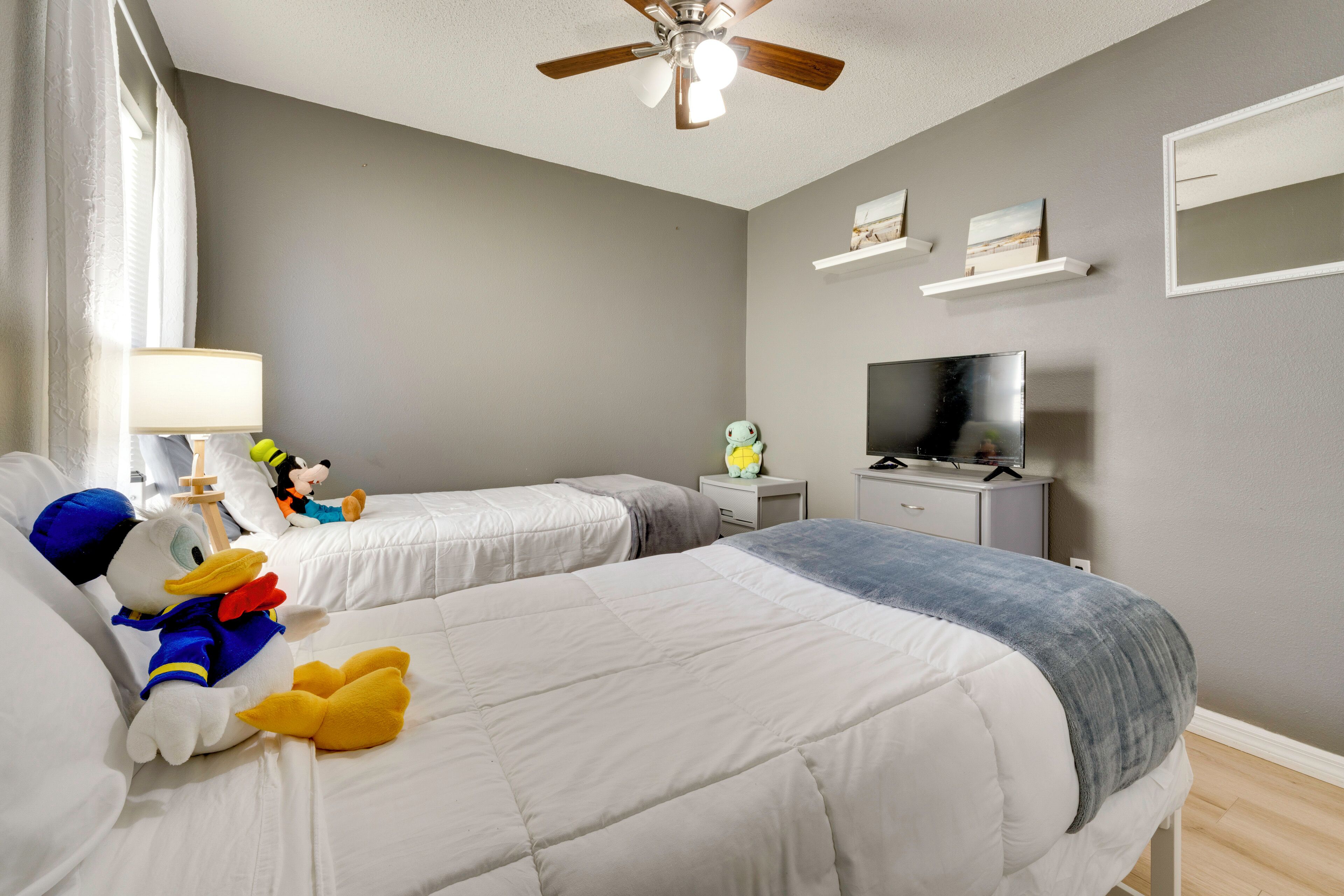 A hotel room with two beds, a ceiling fan, a TV, and a window with curtains.