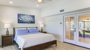 A bedroom with a wooden bed, two bedside tables with lamps, a painting on the wall, and a sliding glass door leading to a balcony. - Group Getaway: Luxe Riverfront Gem in Los Fresnos! (Los Fresnos)
