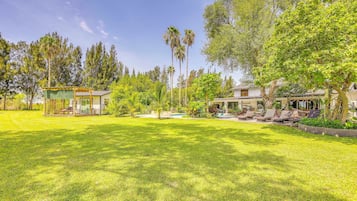 A well-maintained lawn with a pool area, outdoor seating, and a variety of trees and plants.