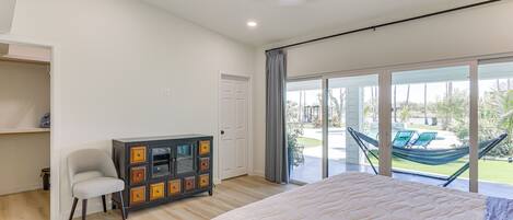 A bedroom with a large bed, a wardrobe, a chair, and a view of a hammock and outdoor seating.