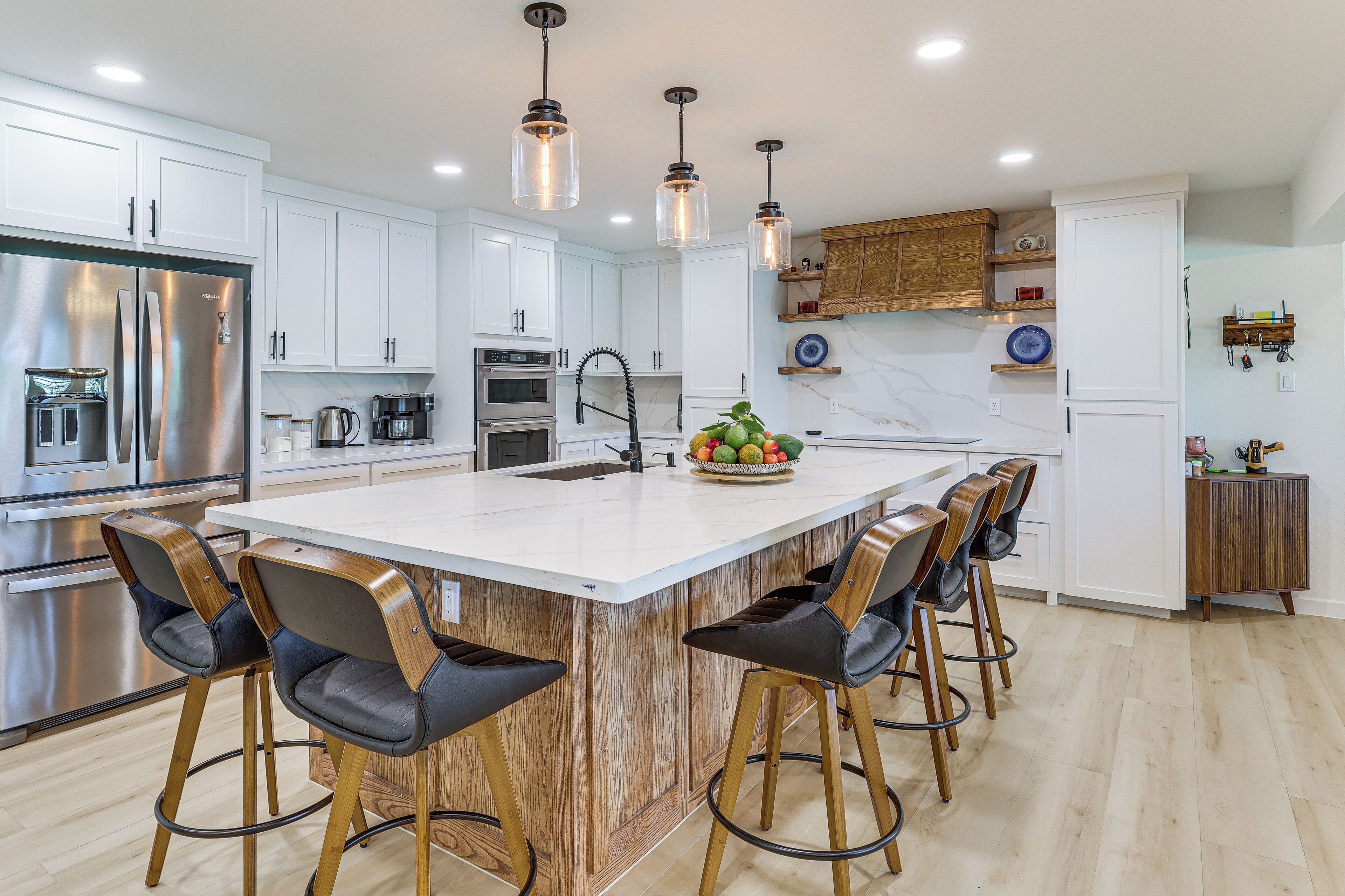 A modern kitchen with white cabinets, stainless steel appliances, and wooden bar stools.