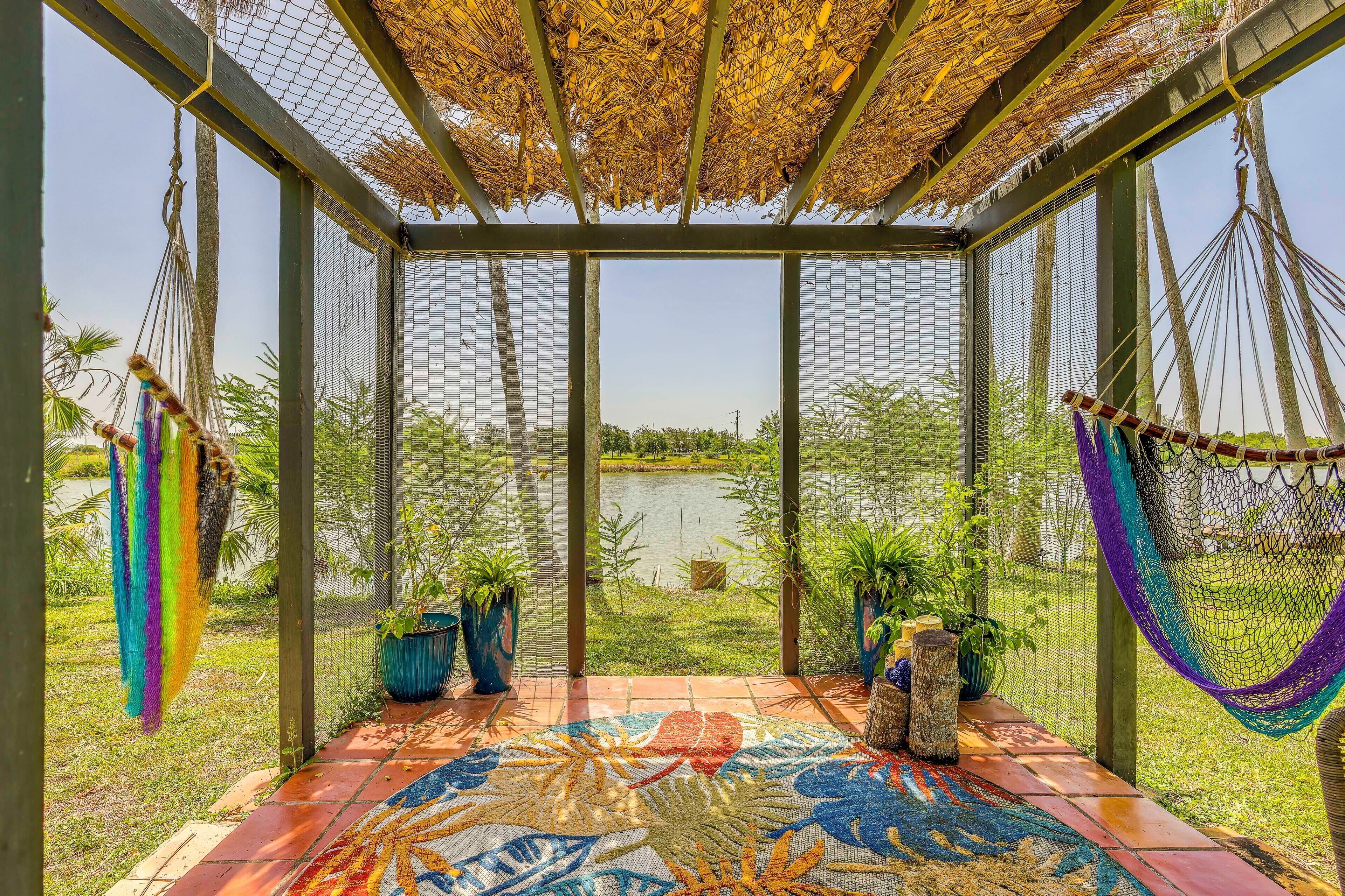 A covered outdoor area with a view of a lake, featuring a hammock, potted plants, and a colorful mosaic floor.