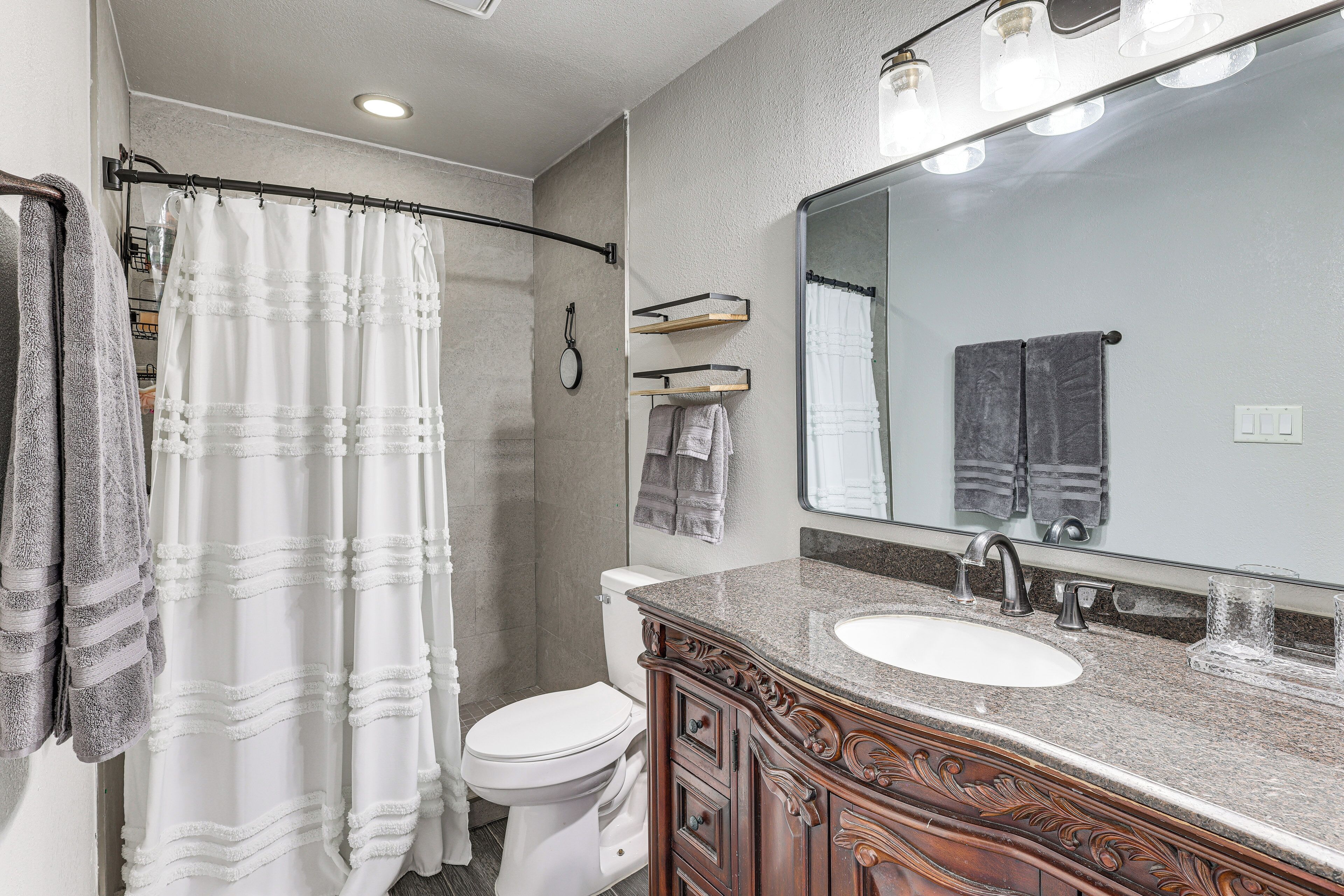 Une salle de bain avec un rideau de douche, des toilettes, un lavabo avec un miroir et des meubles en bois.