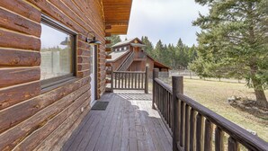 Eine Holzhütte mit einer Holzdar Terrasse, einer Treppe zu einer zweiten Ebene und Blick auf einen bewaldeten Bereich.