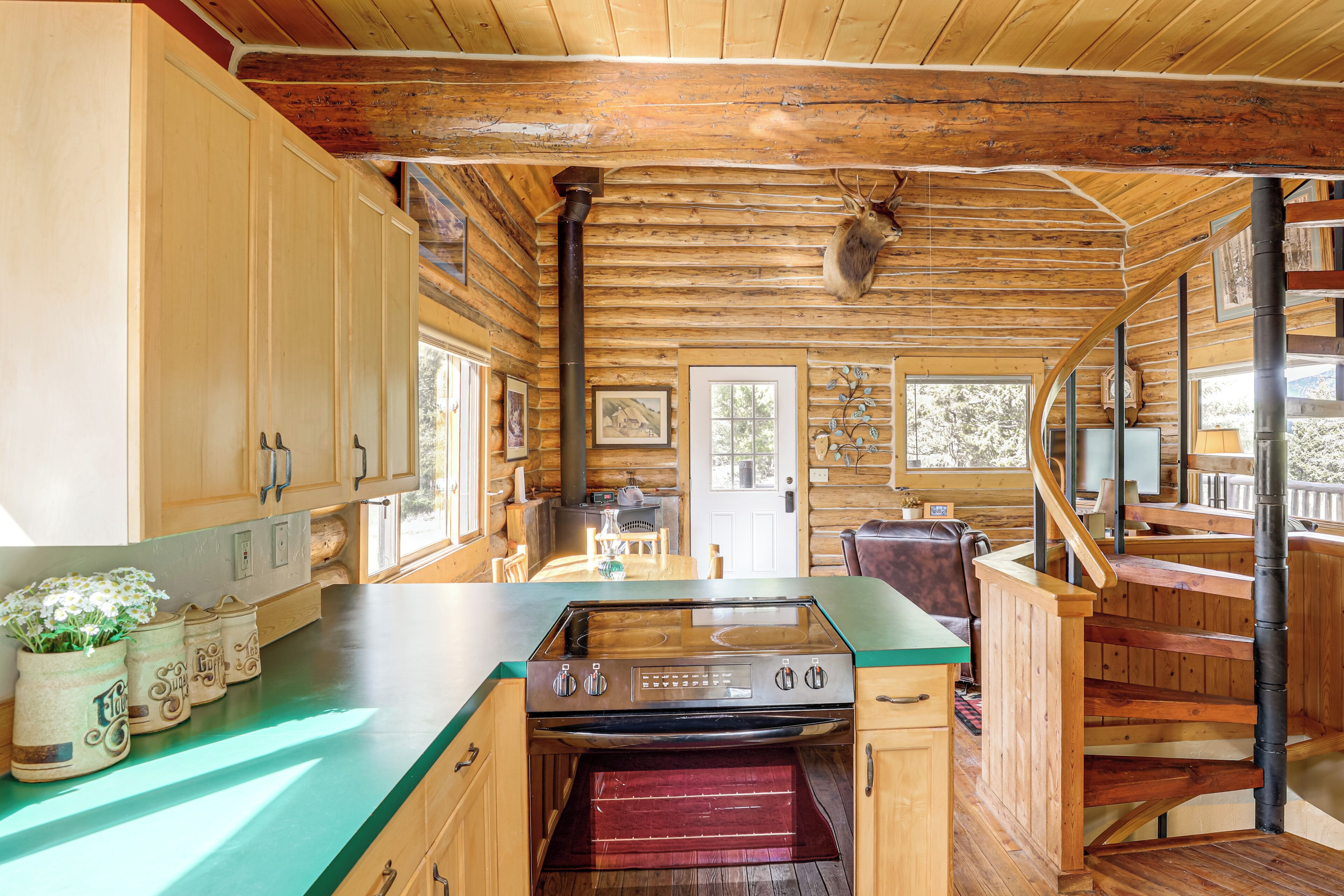 L’intérieur d’une cabane en rondins, avec une cuisine, des murs en bois, un poêle et un escalier.