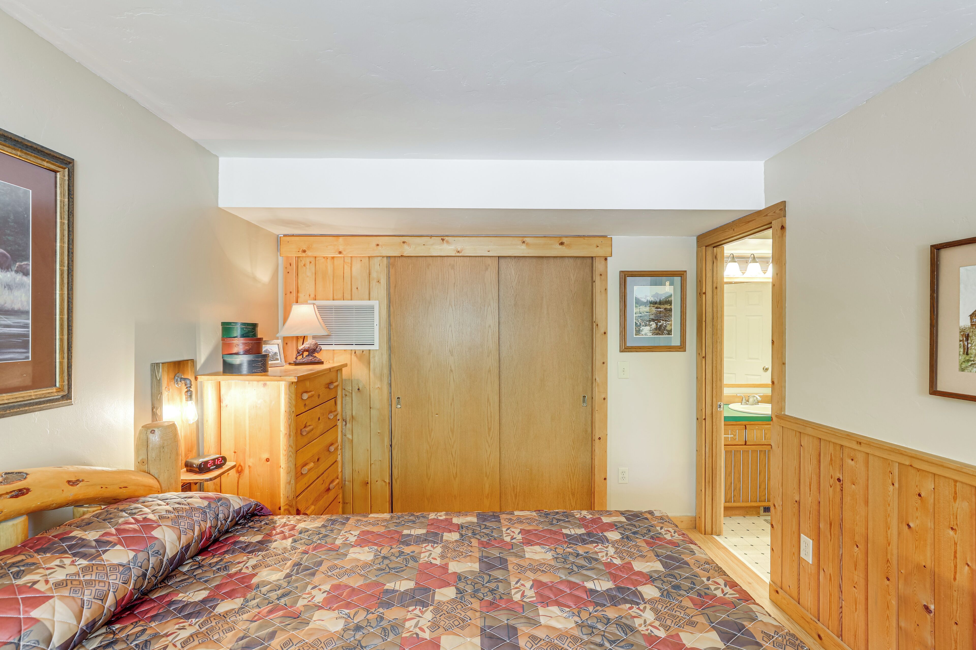 A bedroom with a bed, a wooden wardrobe, a nightstand, a lamp, and a framed picture on the wall.