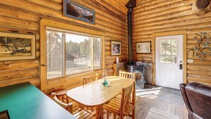 Ein rustikales Blockhaus-Interieur mit Esstisch, Stühlen, Kamin und gerahmten Bildern an den Wänden.