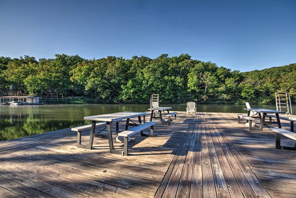 A wooden dock with picnic tables and benches overlooking a calm lake, surrounded by dense forest. - Pet-friendly Lakefront Escape in Osage Beach (Osage Beach)