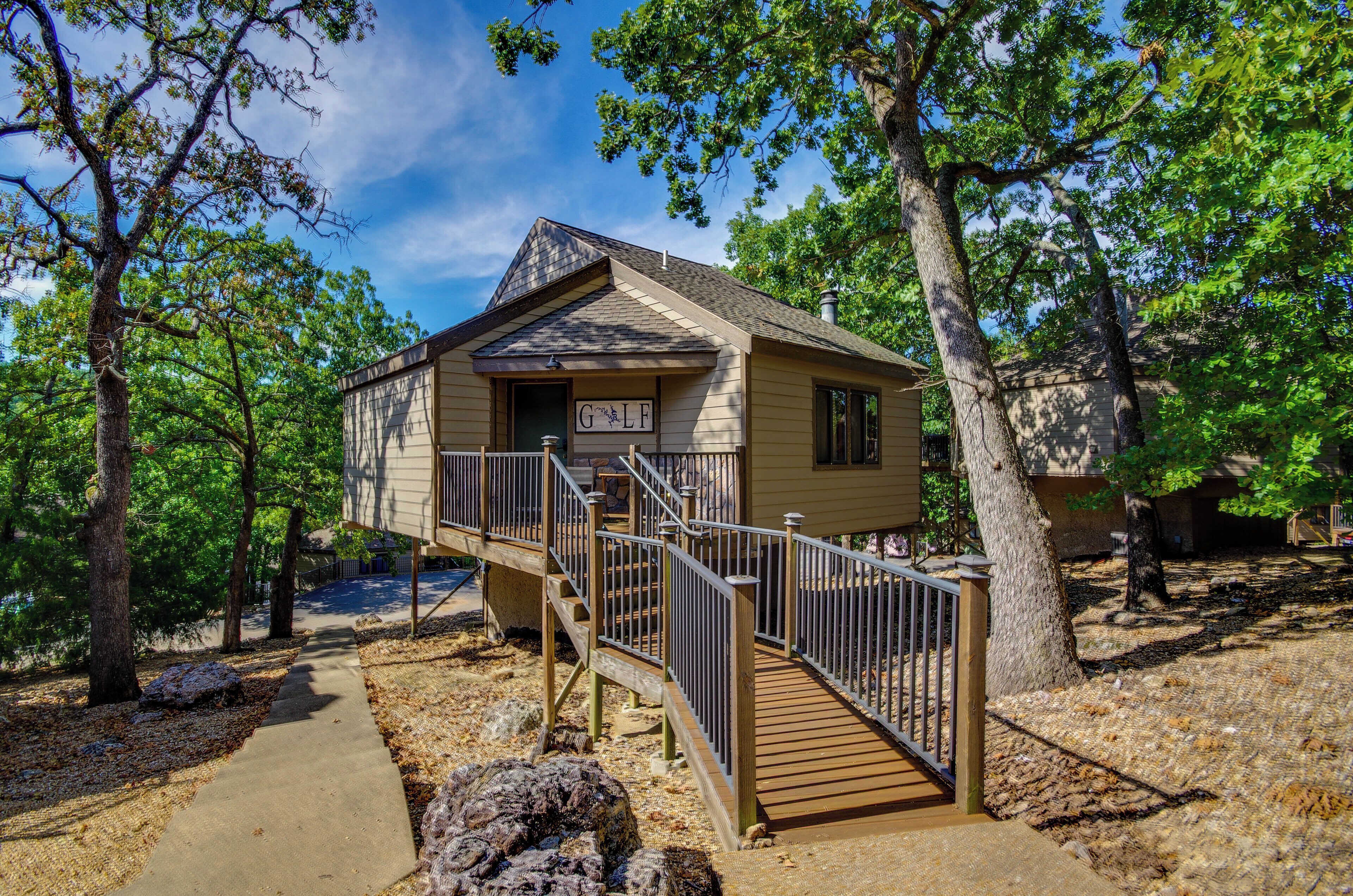 A two-story wooden cabin with a deck and stairs, surrounded by trees.