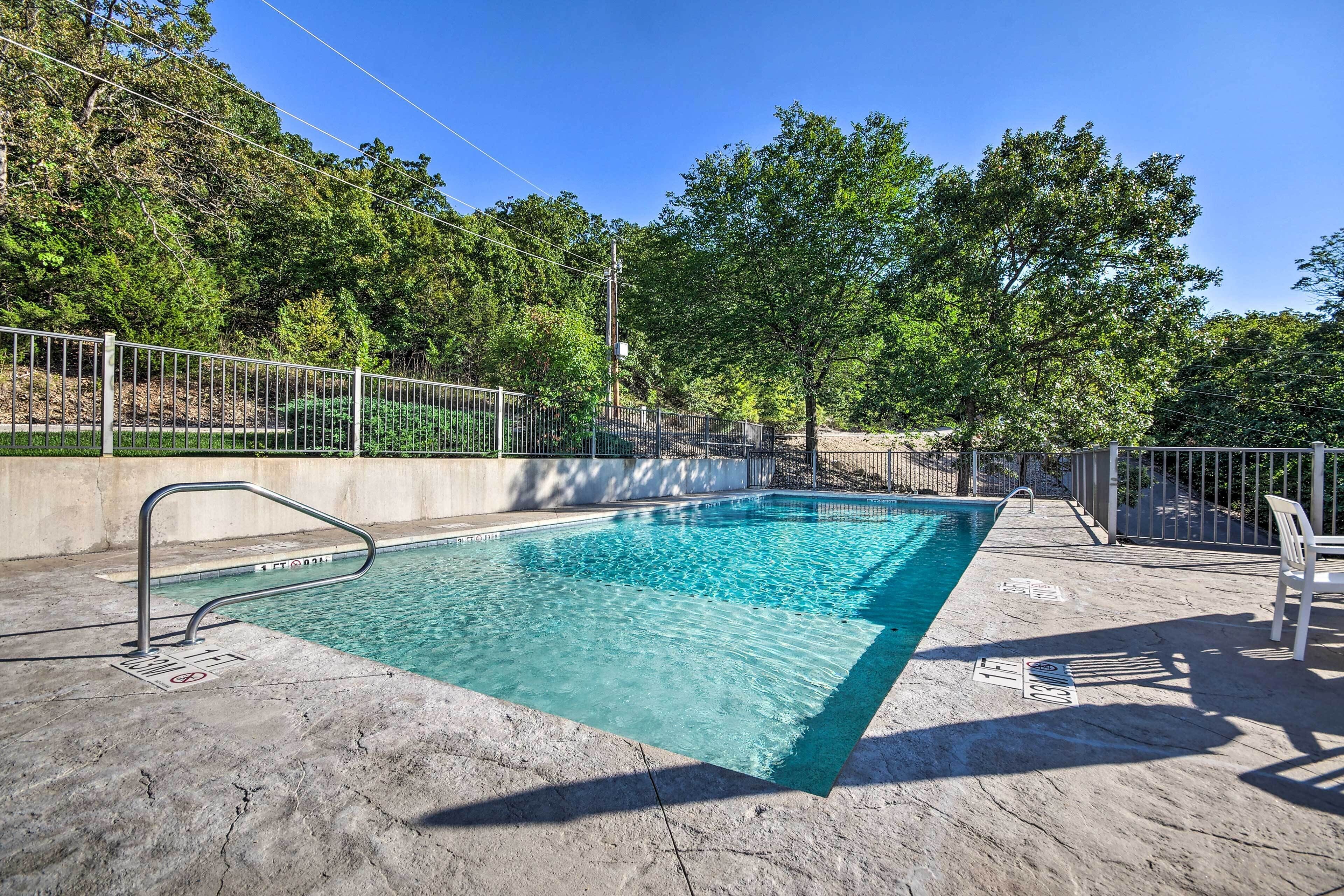 A rectangular swimming pool with a metal ladder and a metal railing on one side, surrounded by trees and a concrete deck.