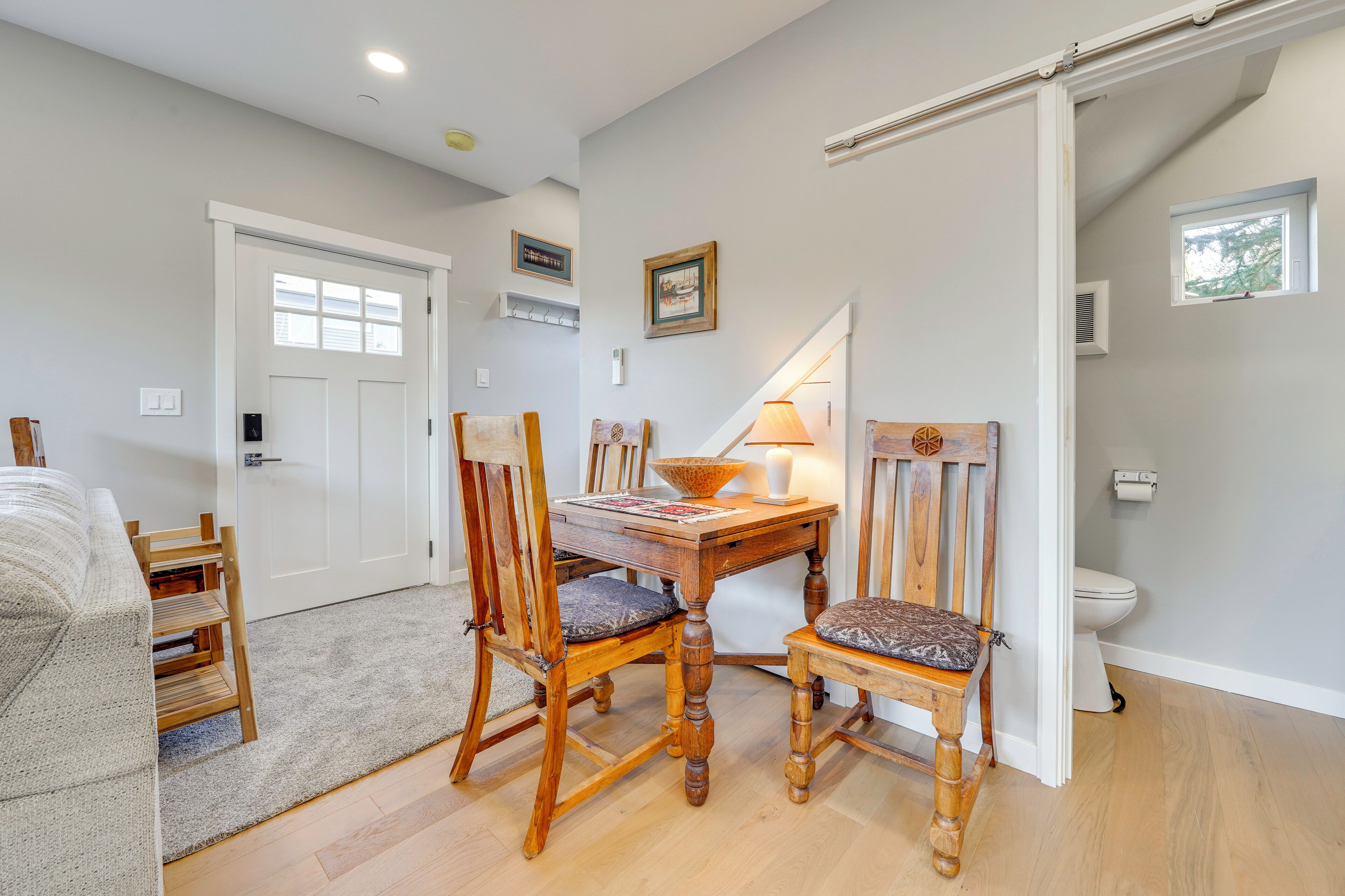 A room with a wooden dining table, two chairs, a sofa, a staircase, and a white door.