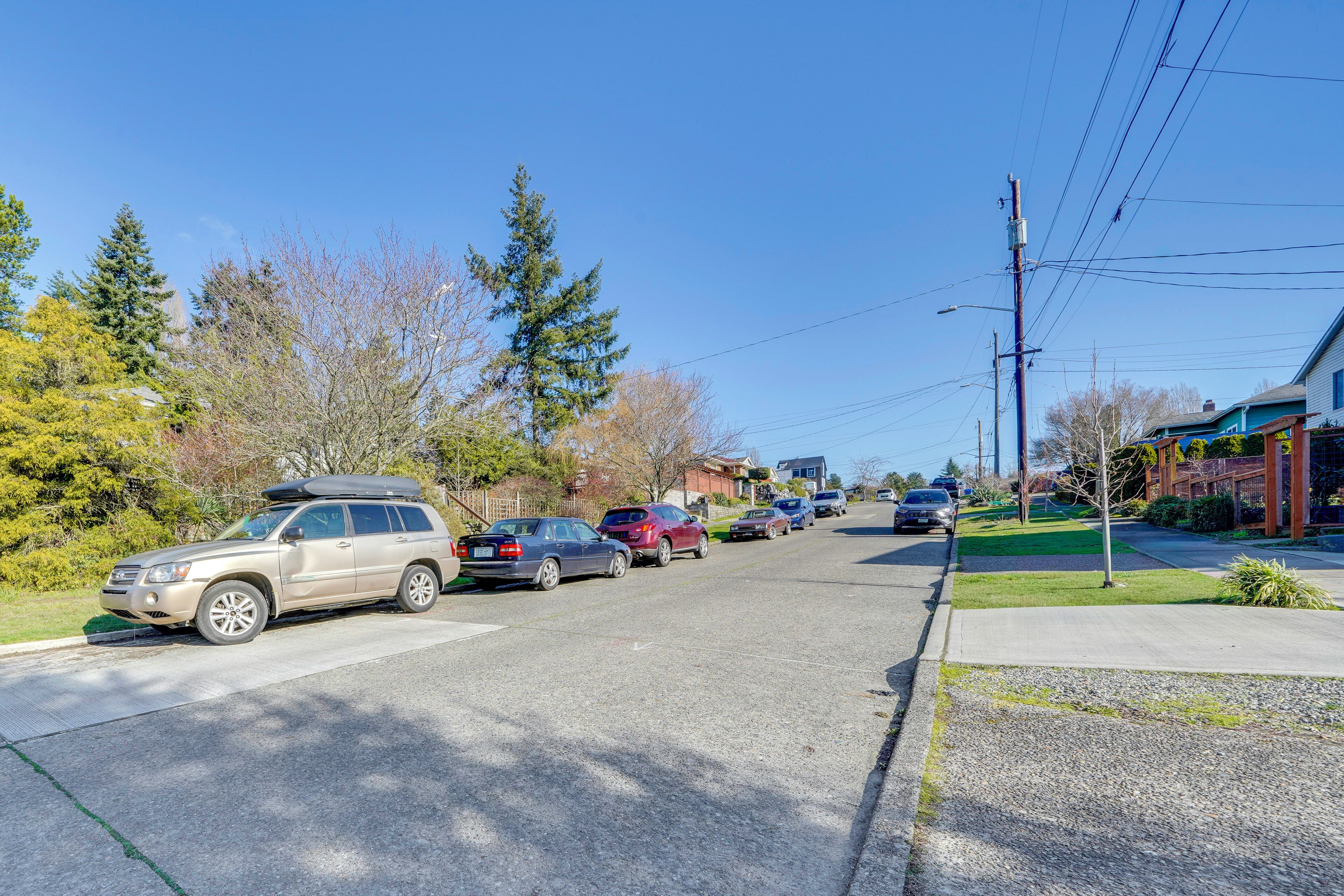 A residential street with parked cars, houses, and trees.