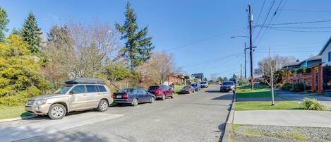 A residential street with parked cars, houses, and trees.