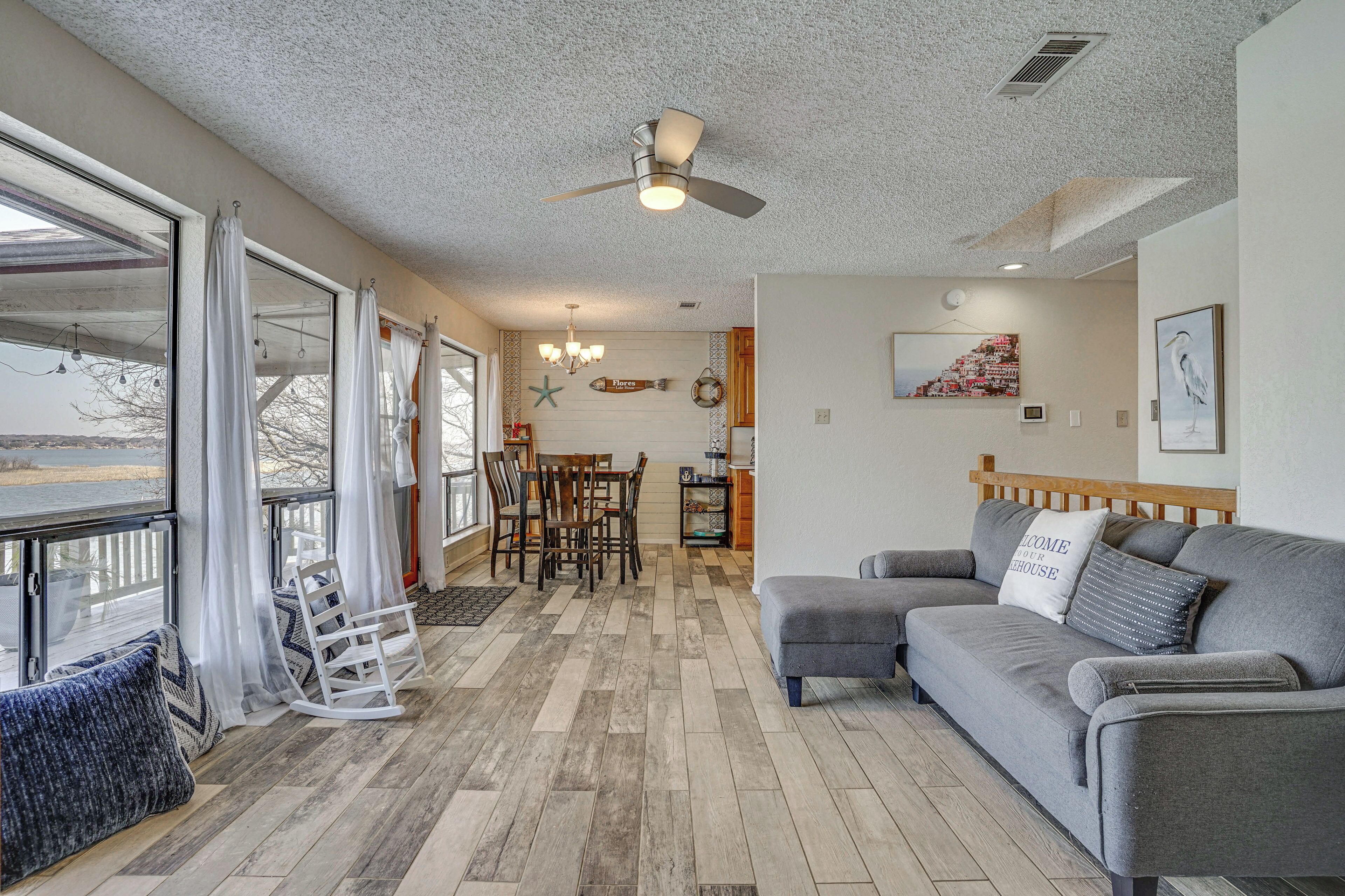 A living room with a gray sofa, a dining area with a wooden table, and a ceiling fan.