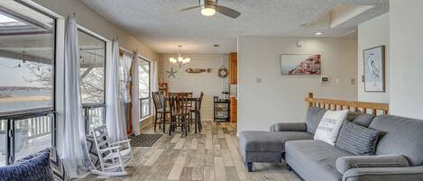 A living room with a gray sofa, a dining area with a wooden table, and a ceiling fan.