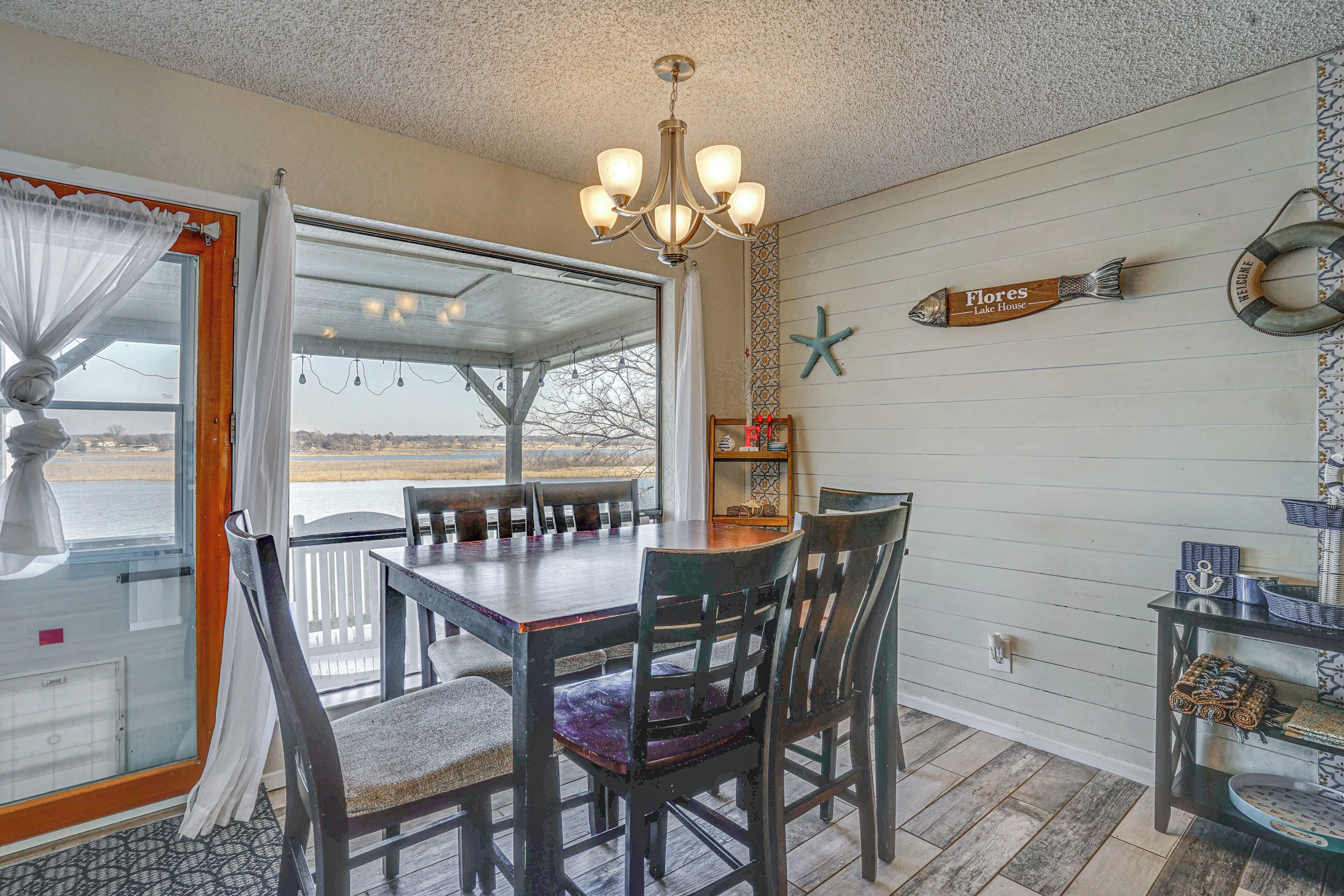 A dining area with a table and chairs, a chandelier, a view through a glass door, and nautical-themed decorations.