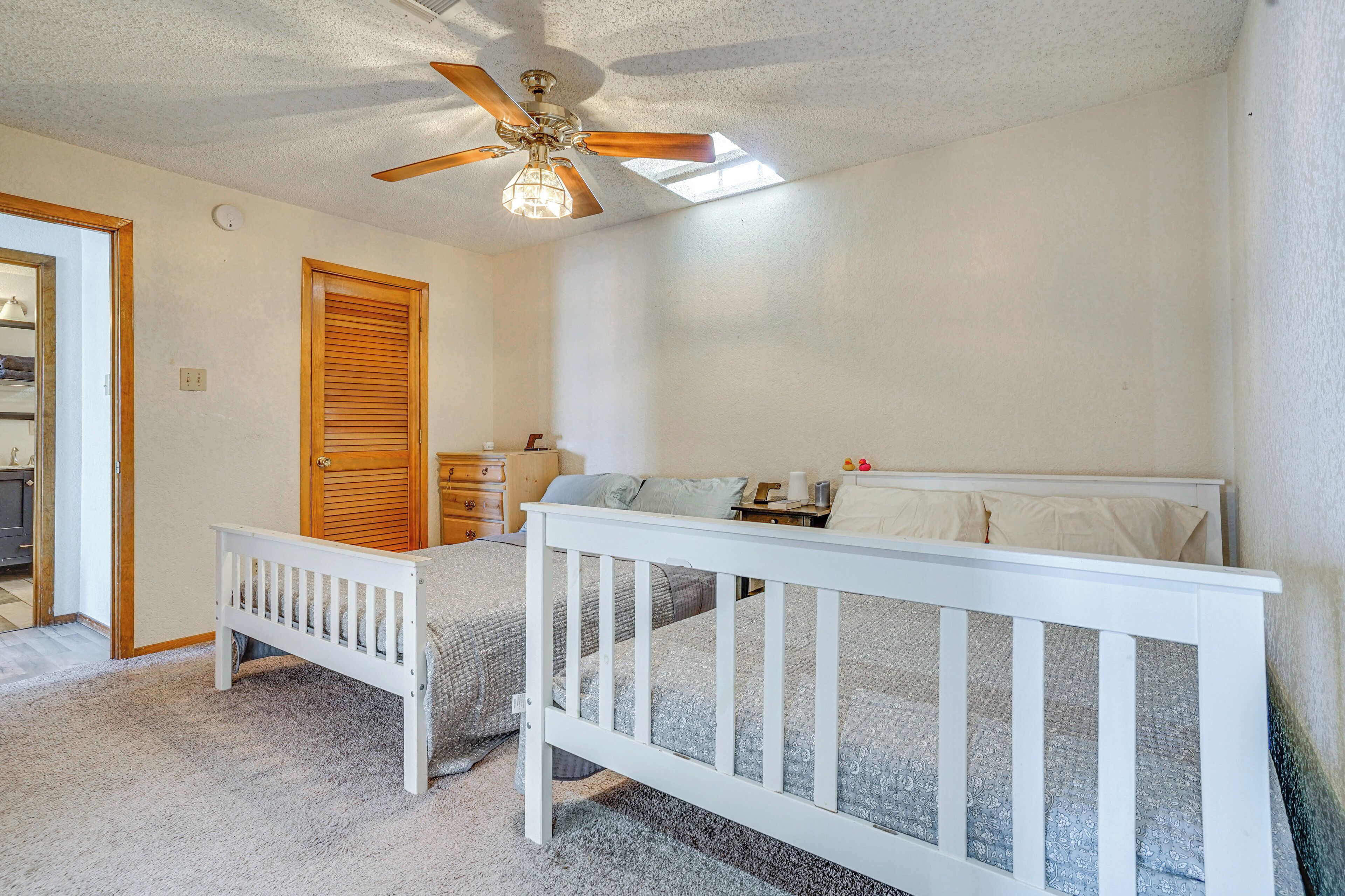 A bedroom with a crib, a wooden door, a ceiling fan, and a nightstand.