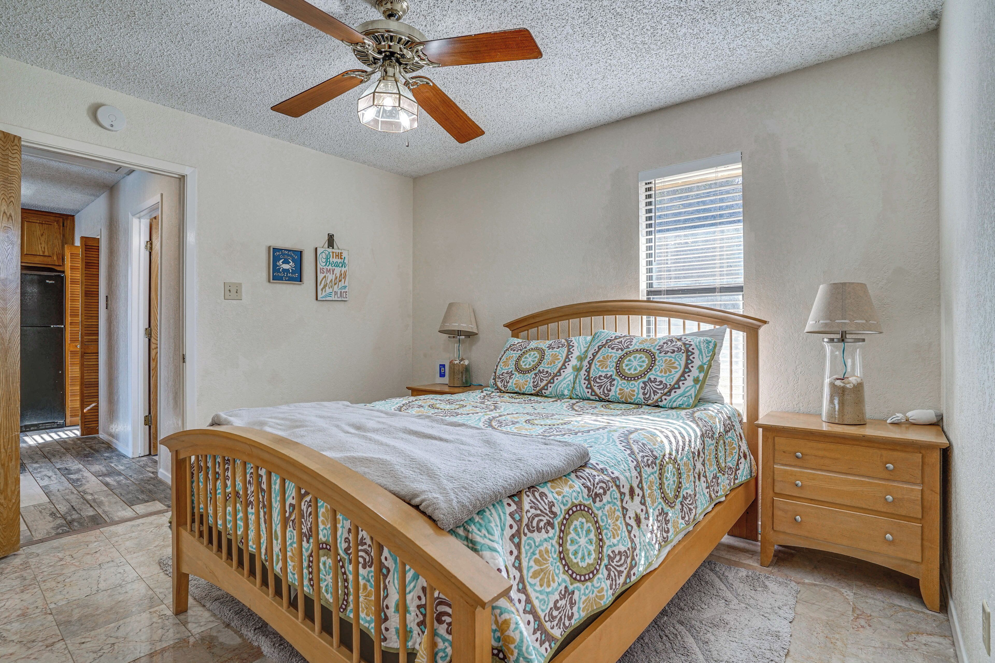 A bedroom with a wooden bed, a ceiling fan, a nightstand, a lamp, and a window with blinds.