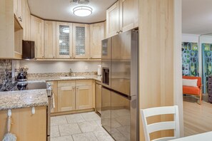 A kitchen with wooden cabinets, a stainless steel refrigerator, granite countertops, and a tiled backsplash. - 2 Mi to Dtwn! Snowbird Gem w/ Pool in Palm Springs (Palm Springs)