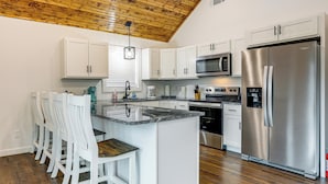 Una cocina con armarios blancos, un refrigerador de acero inoxidable, un microondas y un techo de madera.