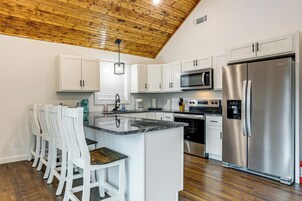 Una cocina con armarios blancos, un refrigerador de acero inoxidable, un microondas y un techo de madera.