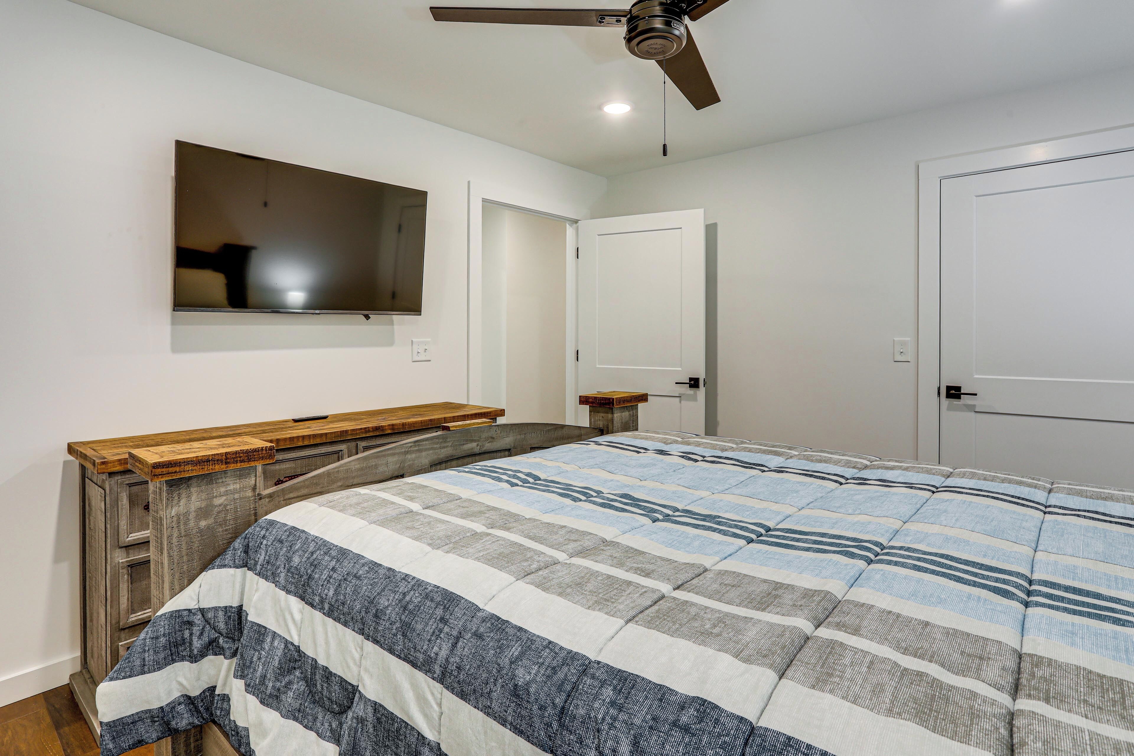 Une chambre à coucher avec un lit, un banc en bois, un ventilateur de plafond, un miroir et une porte.