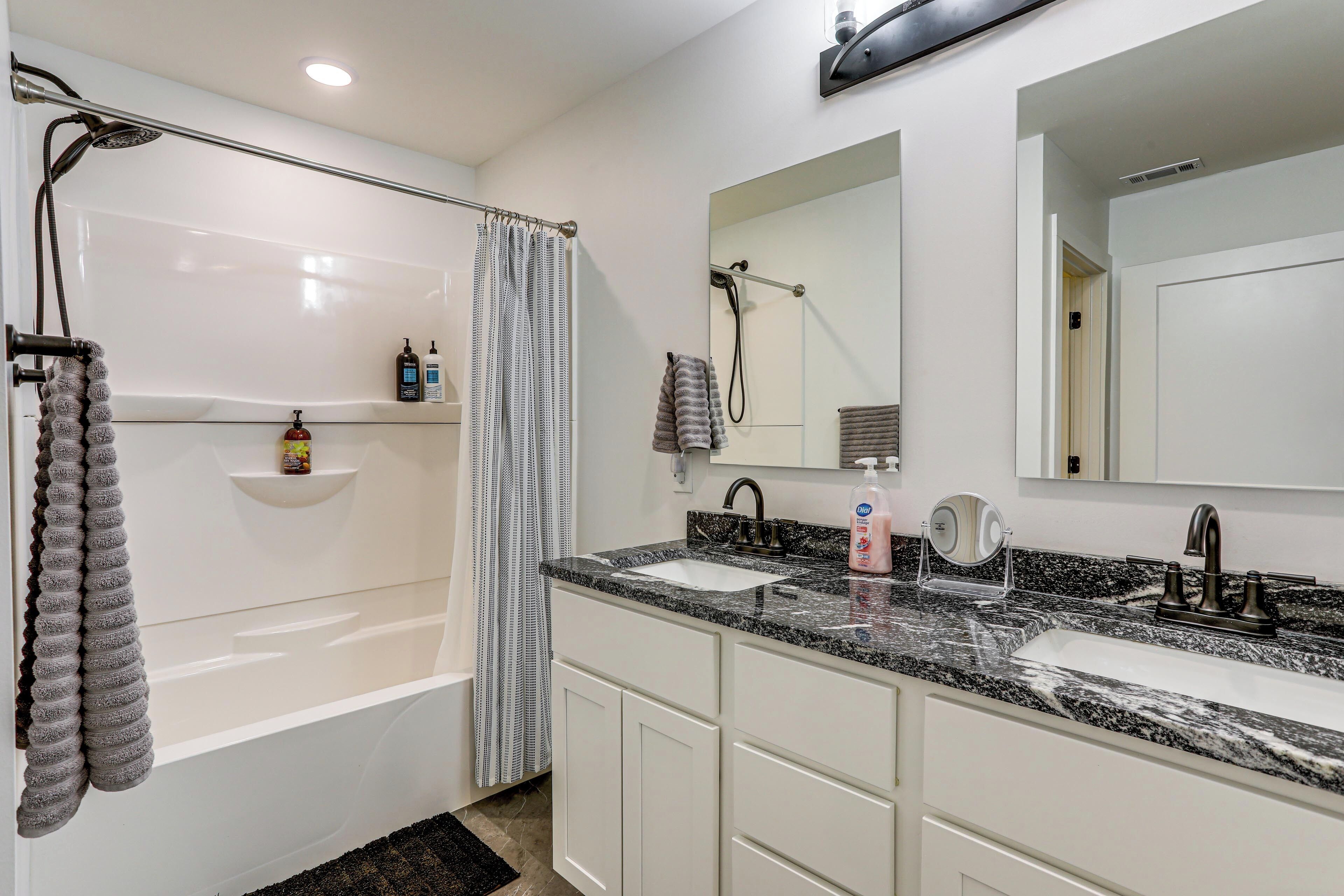 A modern bathroom with a bathtub, two sinks, a large mirror, and a shower.