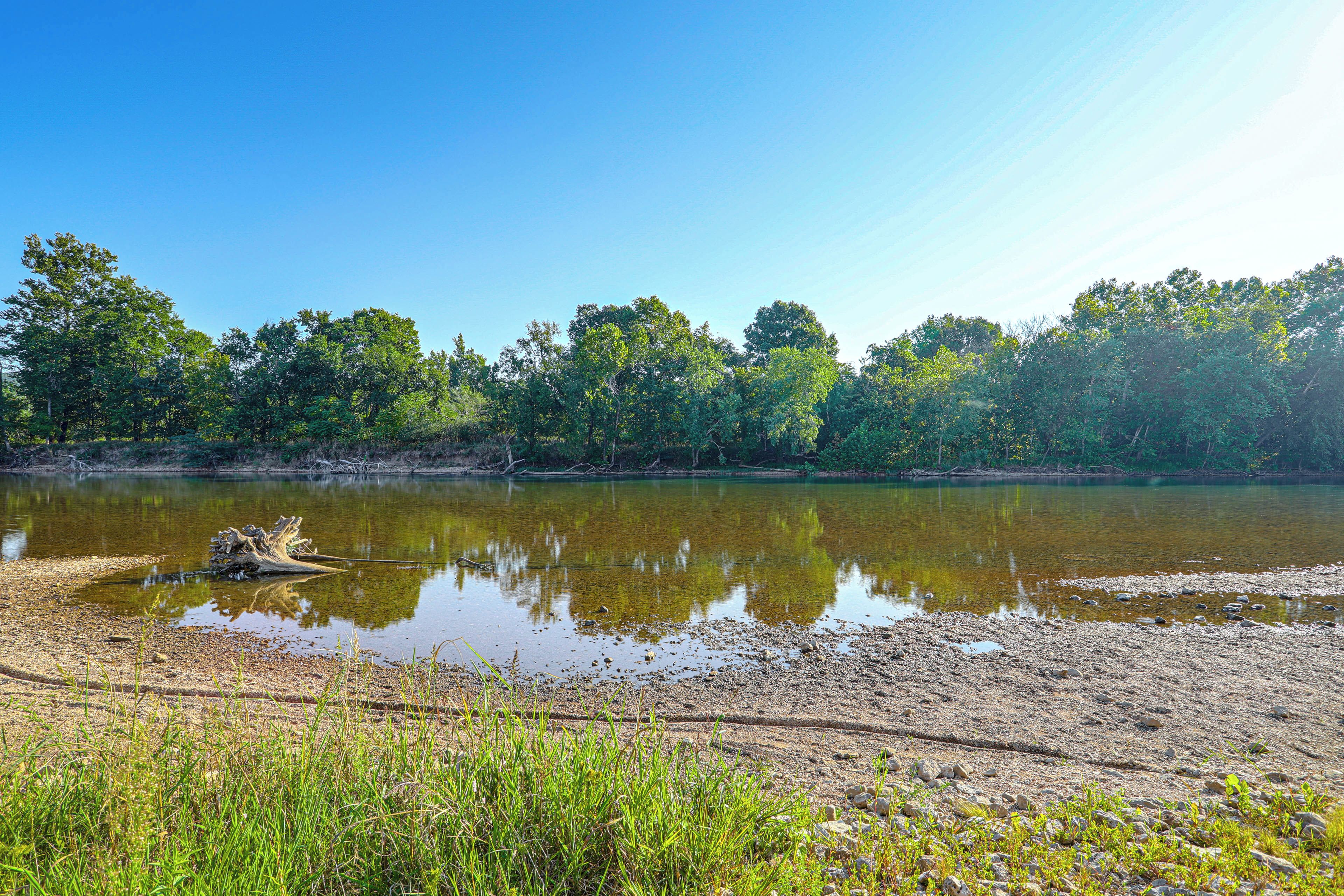 A natural landscape with a calm body of water, trees, and a clear sky.