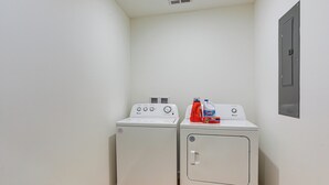 Un cuarto de lavandería con dos electrodomésticos blancos, un cuadro eléctrico en la pared y una puerta.