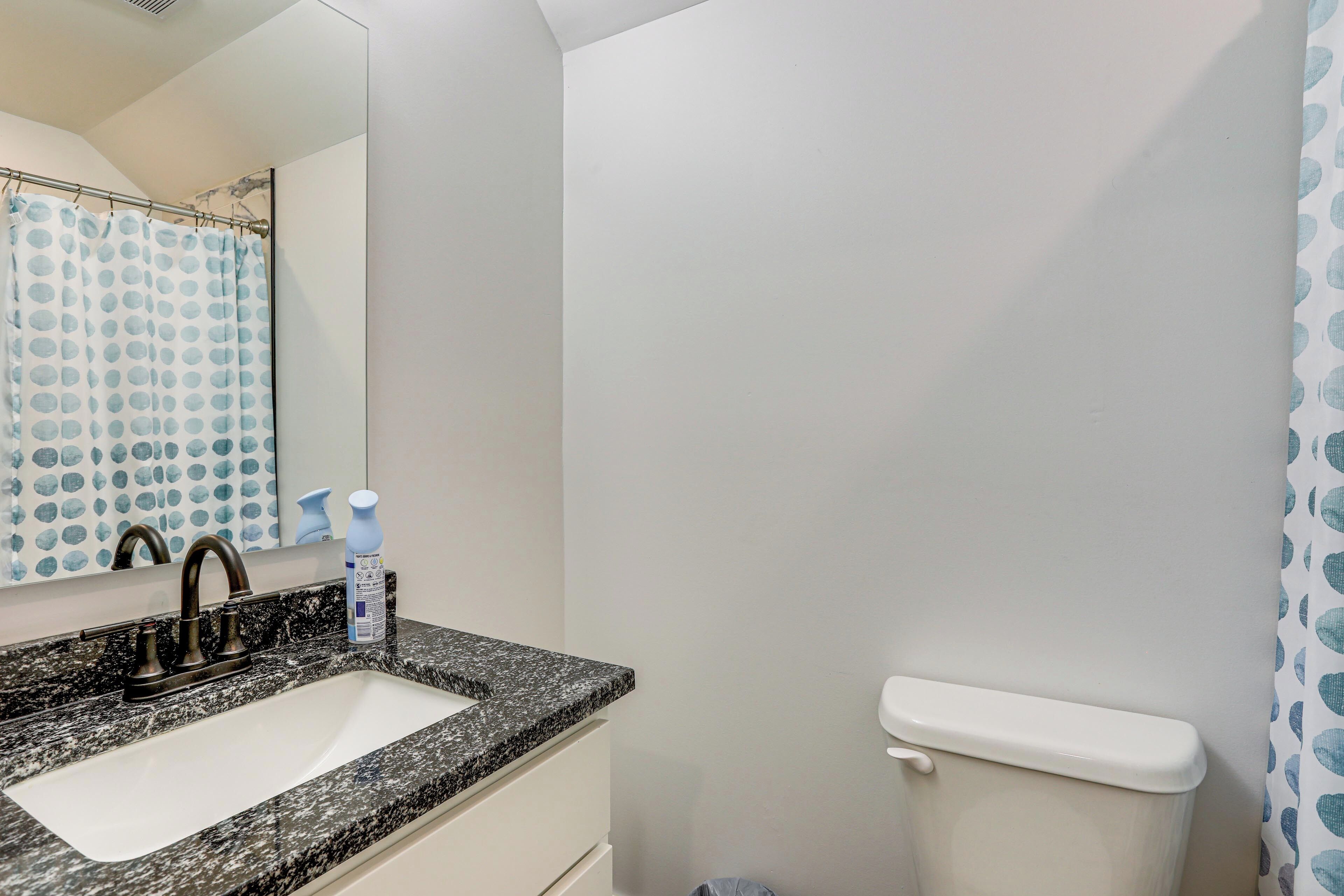A bathroom with a granite countertop sink, a mirror, a toilet, and a shower curtain with a polka dot pattern.