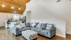 Una sala moderna con un sofá modular, un reposapiés y una cocina al fondo.