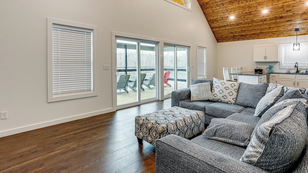 Un salón amplio con un sofá seccional gris grande, techo de madera y vista a una terraza exterior a través de puertas corredizas de vidrio.
