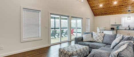 A spacious living room with a large gray sectional sofa, a wooden ceiling, and a view through a sliding glass door to an outdoor deck.