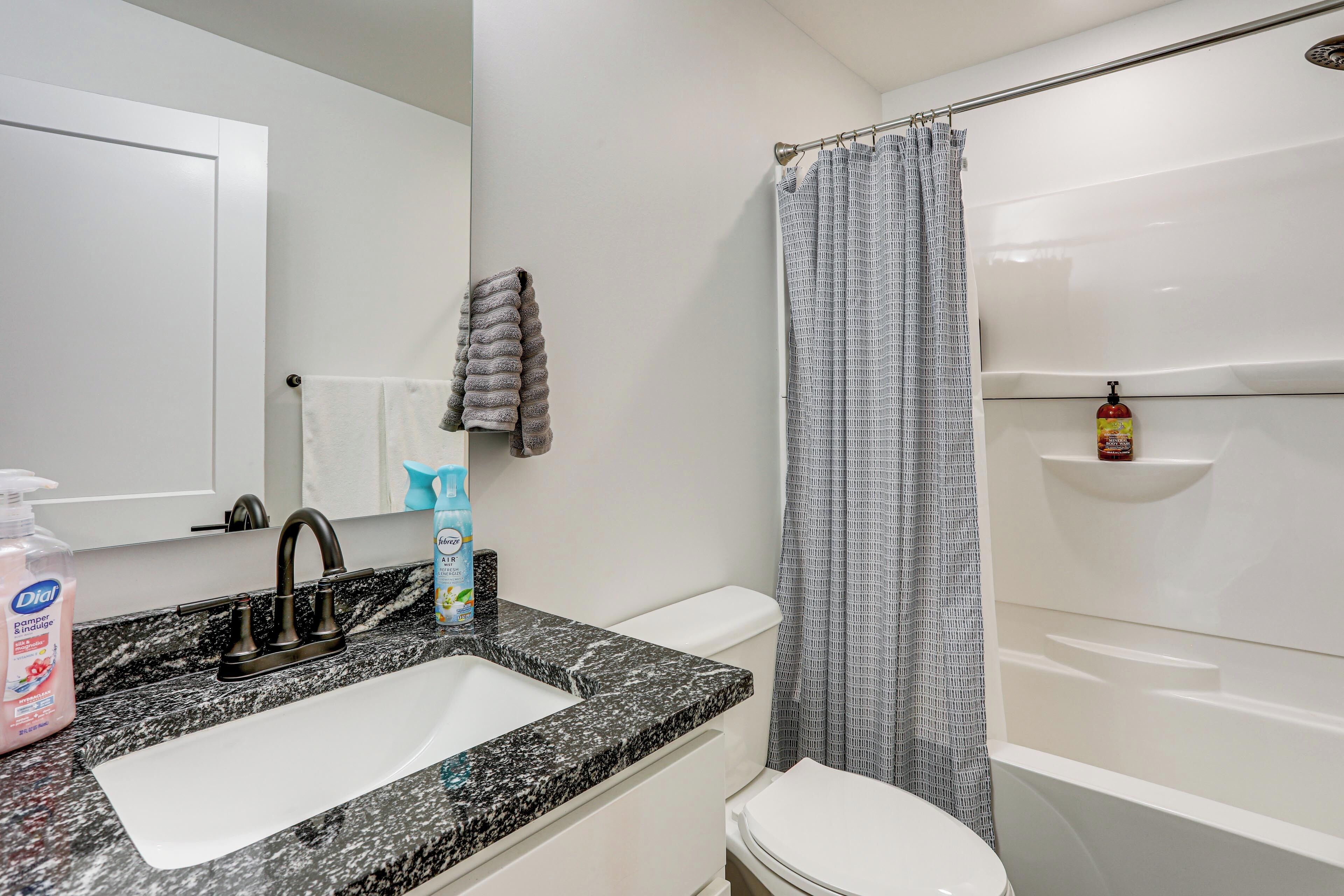 A bathroom with a white sink, dark granite countertop, white toilet, and a shower with a patterned curtain.