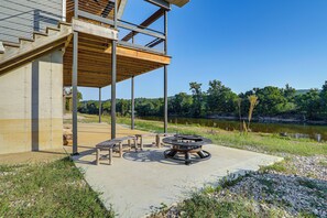 A modern outdoor patio with a fire pit, seating, and a view of a lake.
