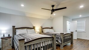 Un dormitorio con dos camas de madera, un ventilador de techo y una mesita de noche con una lámpara.