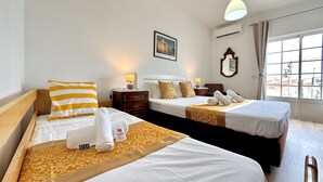 Quarto de hotel com duas camas, uma mesa de cabeceira, abajur, espelho e janela com vista.