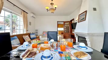 A dining table set with breakfast items, a sofa, and a fireplace in a well-lit room.