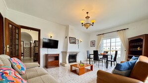 Uma sala de estar com sofá, poltrona, televisão, lareira, mesa de jantar e cadeiras.