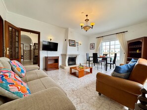 Ein Wohnzimmer mit Sofa, Sesseln, Fernseher, Kamin, Esstisch und Stühlen.