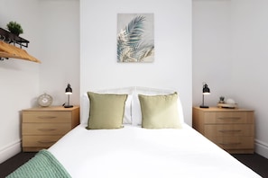 A bedroom with a bed, two nightstands, a wall-mounted shelf with a plant, and a wall art piece. - Spacious 6-Bed Home for Work Crews & Groups (Brynmill)