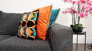 A grey sofa with two patterned cushions and a potted orchid plant.