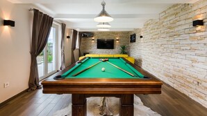 A pool table in a room with a brick wall, a television mounted above it, and a sofa in the background. - Beautiful apartment near the beach with pool (Crikvenica)