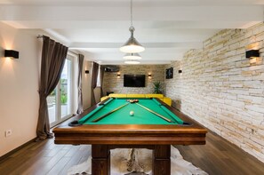 A pool table in a room with a brick wall, a television mounted above it, and a sofa in the background. - Beautiful apartment near the beach with pool (Crikvenica)