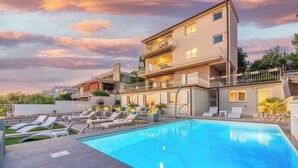 A modern two-story building with a swimming pool, lounge chairs, and a stone facade. - Beautiful apartment near the beach with pool (Crikvenica)