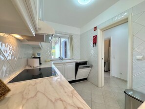 Une cuisine avec des meubles blancs, un plan de travail en marbre, une fenêtre et un détecteur d’incendie rouge.