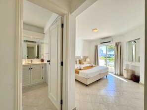 Une chambre avec un grand lit, une salle de bain avec un miroir et un lavabo, et une vue sur l’extérieur grâce à une porte vitrée.