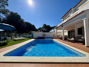 A swimming pool with a tiled edge, surrounded by a patio area with chairs and a table. - VILAMOURA SUMMER VILLA 3 WITH POOL by HOMING (Vilamoura)