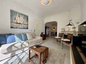 A living room with a sofa, coffee table, and a painting of sailboats. There is a dining area with chairs and a table. - VILAMOURA SUMMER VILLA 3 WITH POOL by HOMING (Vilamoura)
