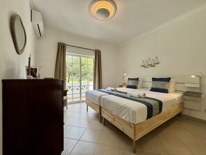 A bedroom with a wooden bed, a nightstand, a desk, a chair, a large window with curtains, and a ceiling light fixture. - VILAMOURA SUMMER VILLA 3 WITH POOL by HOMING (Vilamoura)